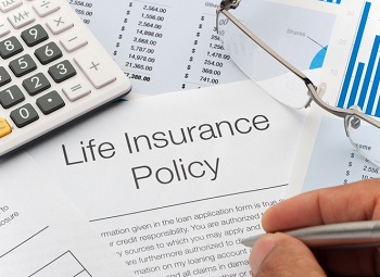A life insurance policy page surrounded by a calculator, glasses and other papers